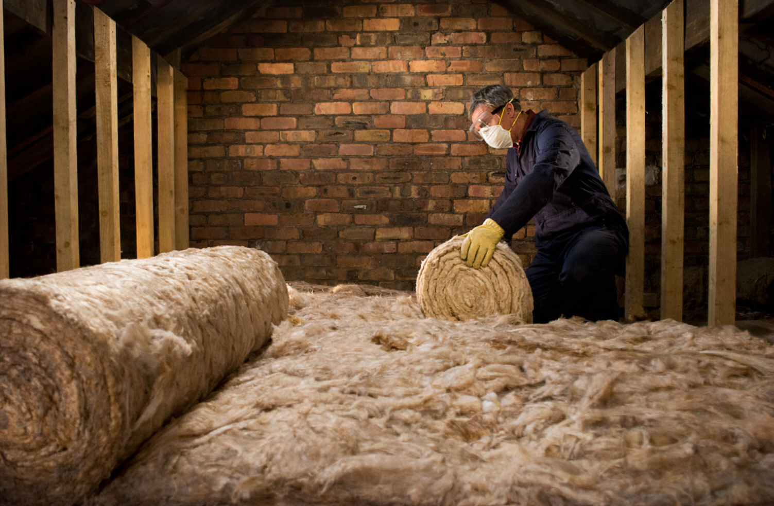 Worker with face mask laying roll of loft insulation.